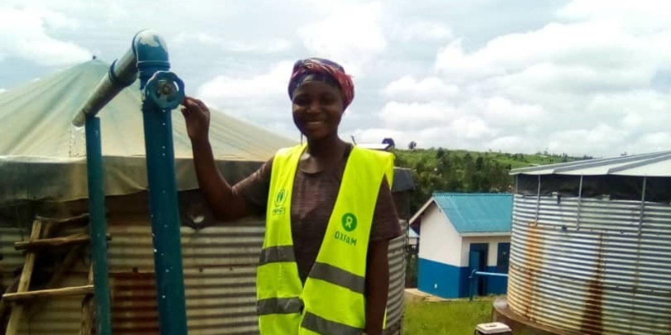 Tantine standing next to reservoir tank at her work station at Sweswe Pump Station. Photo by Joyce Amuron, Oxfam.jpg